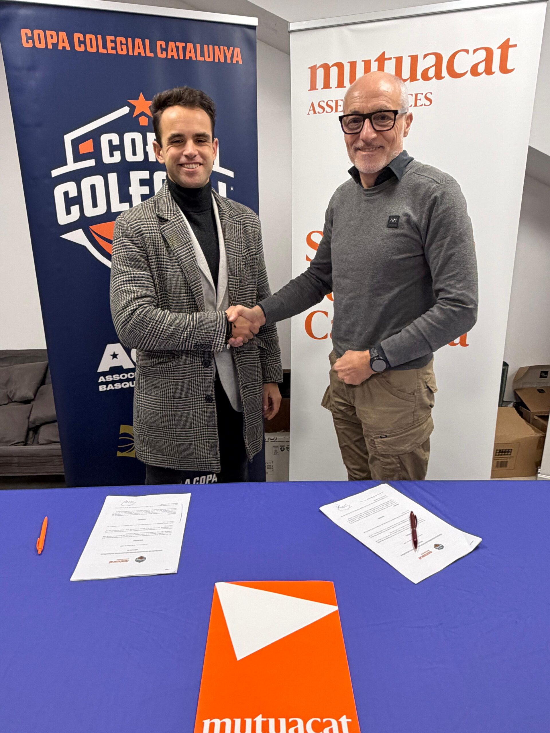 Sergi Àlex Bañon i Leo Martínez Regales somrients fan una encaixada de mans durant la formalització de l'acord entre Copa Co·legial Catalunya i Mutuacat